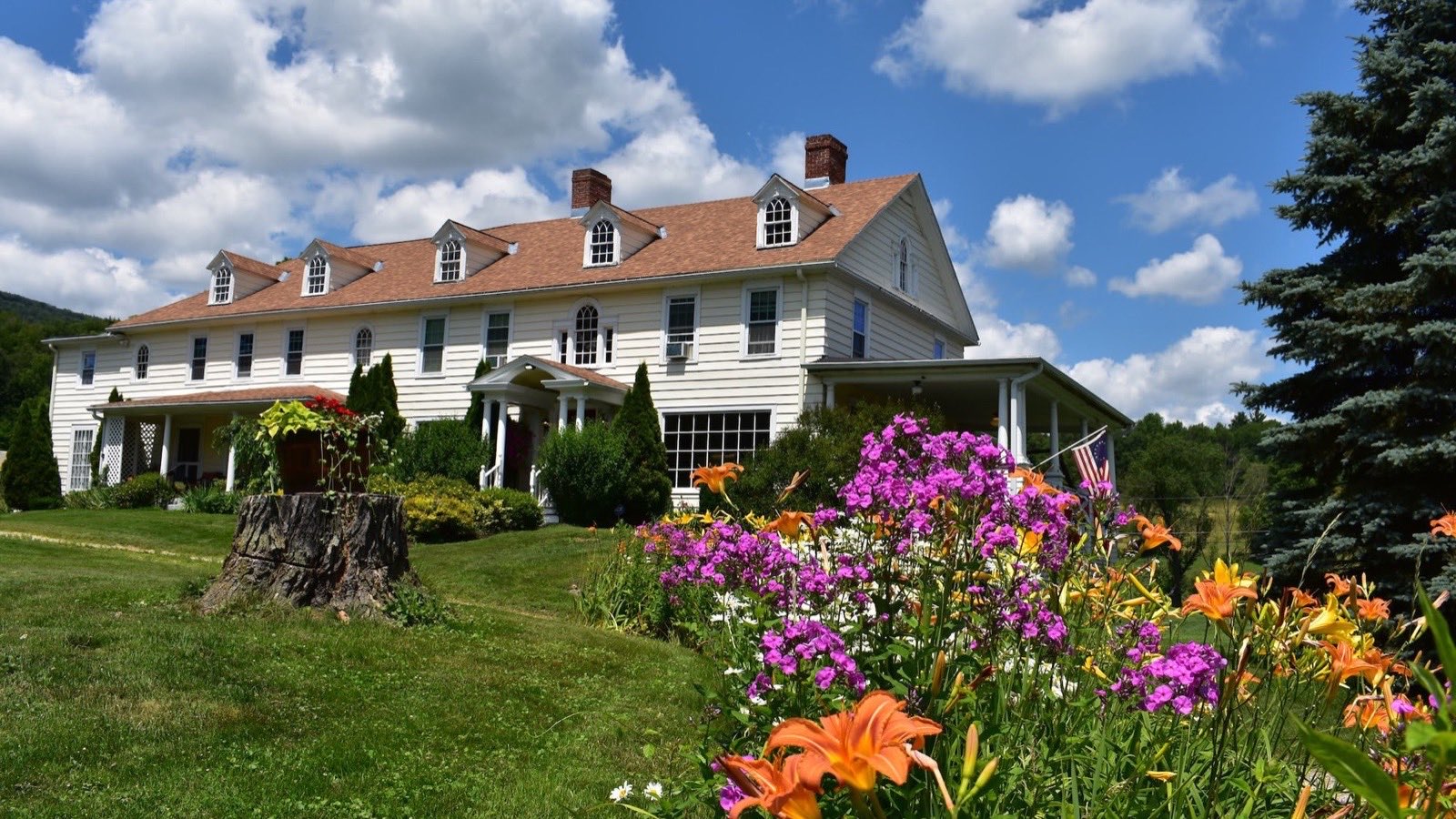 The Harbour House Inn, a white 1793 farmhouse, behind a garden of lilies and phlox in spring.